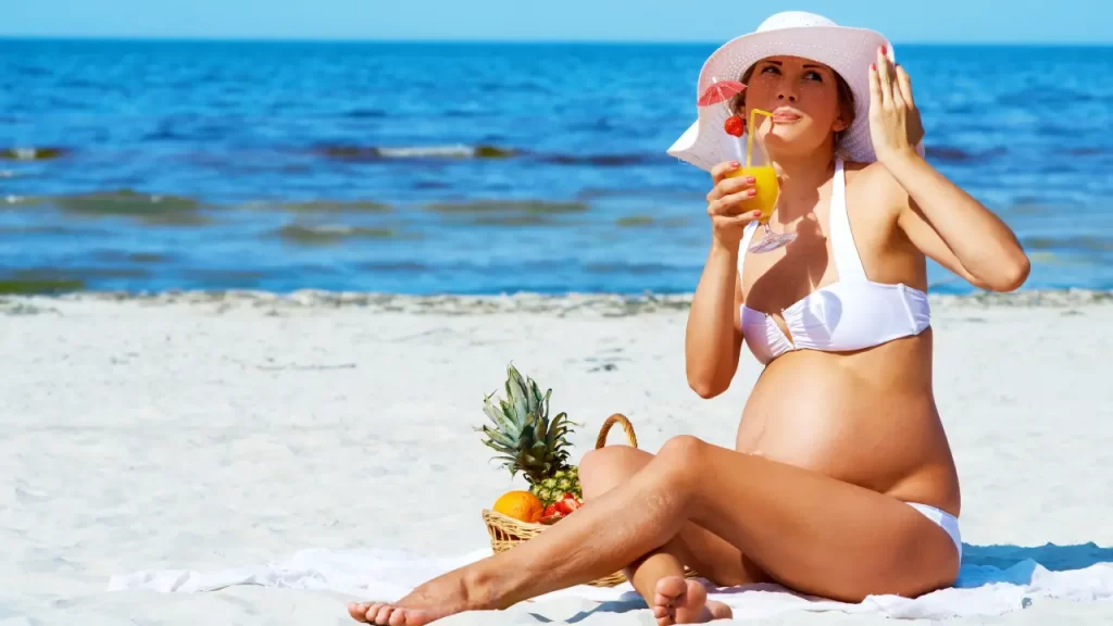 gestante na praia com drink e frutas