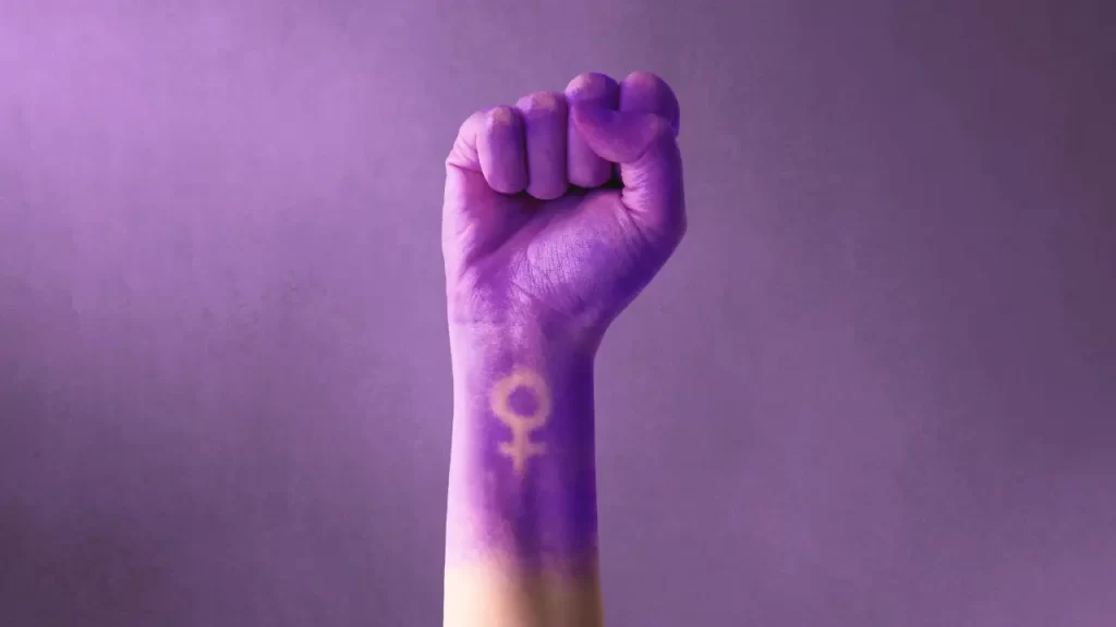 mão tingida de roxo com o símbolo de feminino e punho cerrado