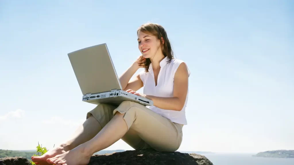 mulher com laptop sorrindo sentada em uma pedra