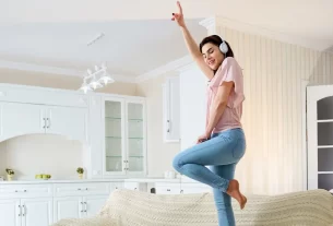 mulher dançando com fones de ouvido em cima do sofá