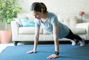 Mulher madura de 45 anos fazendo exercícios de calistenia em casa, demonstrando prancha com postura correta