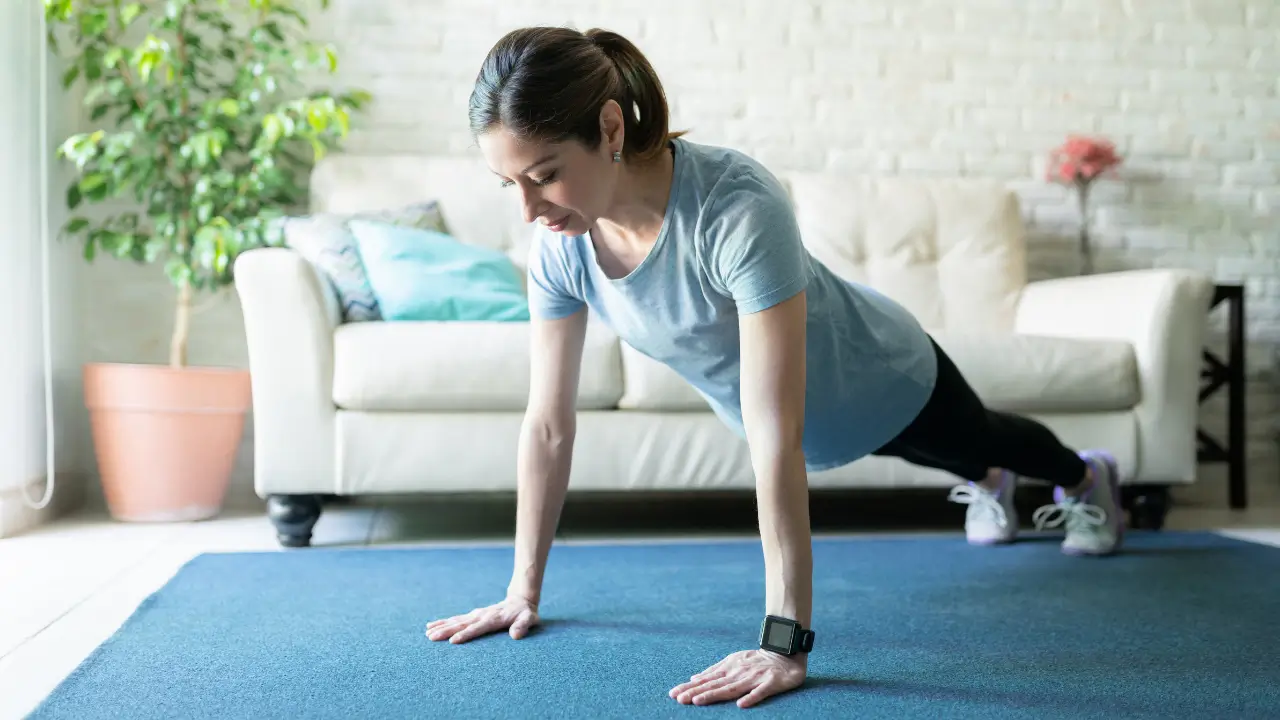 Mulher madura de 45 anos fazendo exercícios de calistenia em casa, demonstrando prancha com postura correta