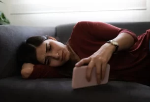 Mulher madura usando smartphone olhando pensativa, representando reflexão sobre stalkear nas redes sociais