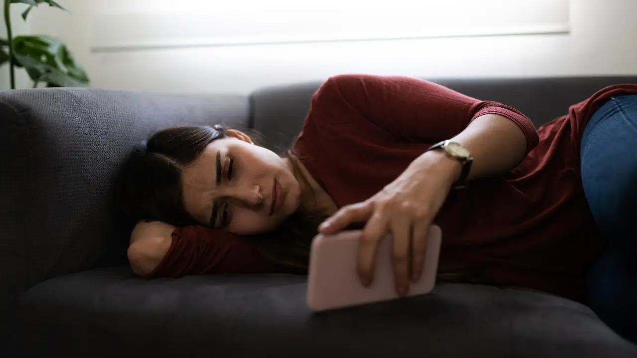 Mulher madura usando smartphone olhando pensativa, representando reflexão sobre stalkear nas redes sociais