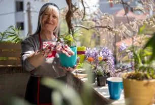 Mulher cuidando de plantas em jardineiras na varanda, demonstrando os benefícios da jardinagem para o bem-estar