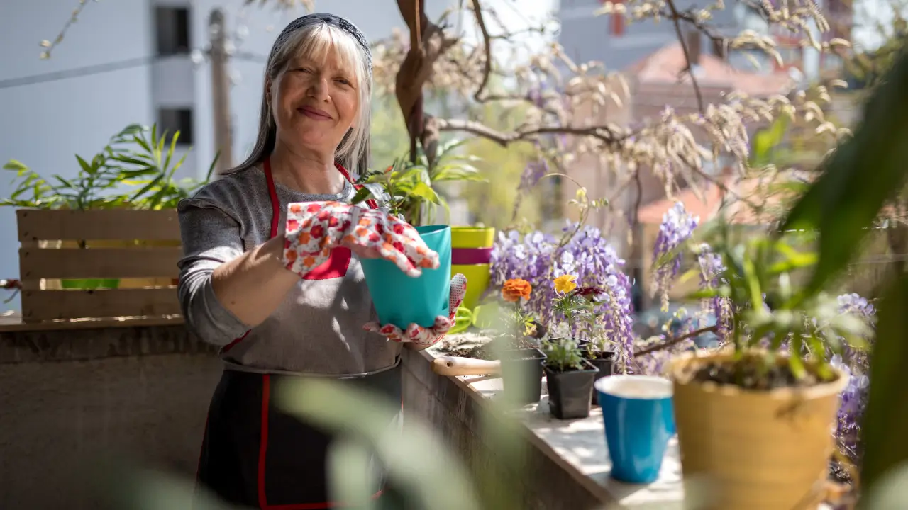 Mulher cuidando de plantas em jardineiras na varanda, demonstrando os benefícios da jardinagem para o bem-estar