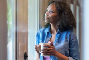 Mulher pensativa olhando pela janela, refletindo sobre pensar em tempos de IA e preservar essência humana